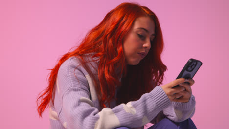 Studio-Shot-Of-Young-Gen-Z-Woman-Gaming-Streaming-Or-Using-Social-Media-On-Mobile-Phone-Against-Pink-Background